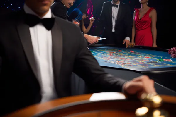 A professional dealer in a tuxedo greeting players at the roulette table, symbolizing the authentic live casino feel at TIKLUCK.